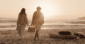 Couple walking on the sandy beach in Carmel at sunset, carrying a picnic basket toward a glowing fire pit.